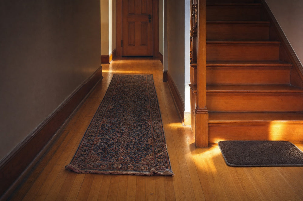 A runner rug and a non-slip mat laid down a hallway at the foot of the stairs