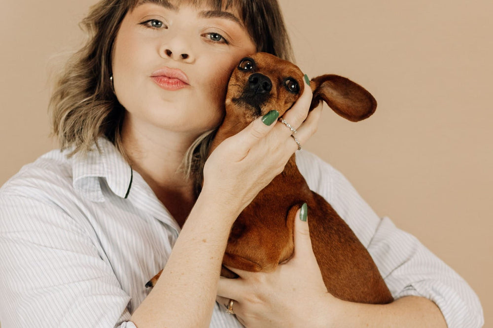 A woman holding a red smooth-coated Dachshund close.