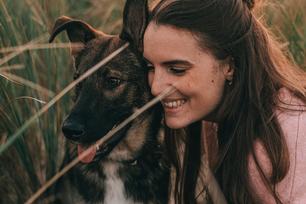 A woman embracing a black-and-tan German Shepherd in sunlit grass.
