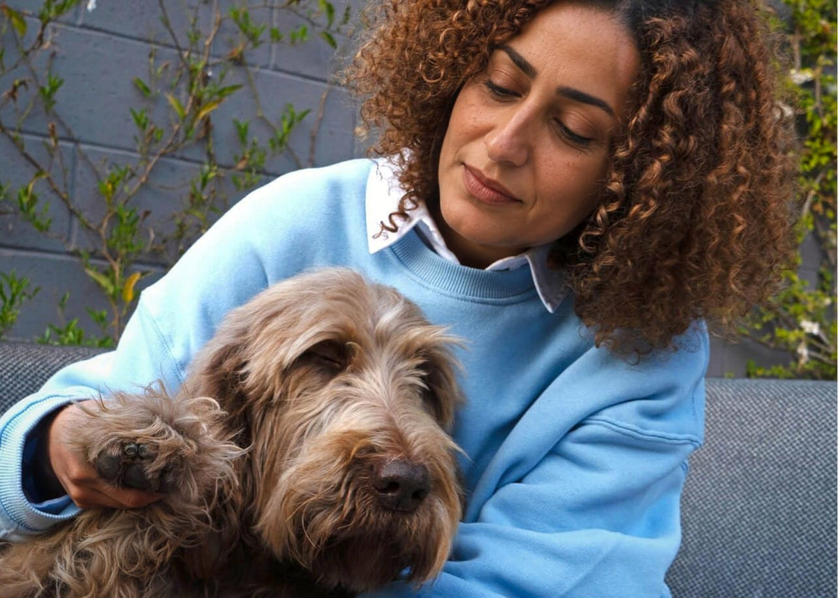 A woman sits with her shaggy dog held close on an outdoor sofa