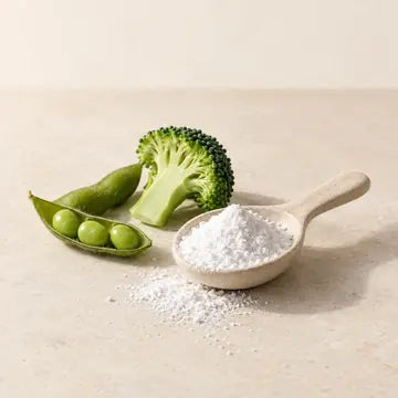 Fine poudre blanche de NMN dans une cuillère en céramique, à côté d’un fleuron de brocoli et d’une cosse d’edamame.
